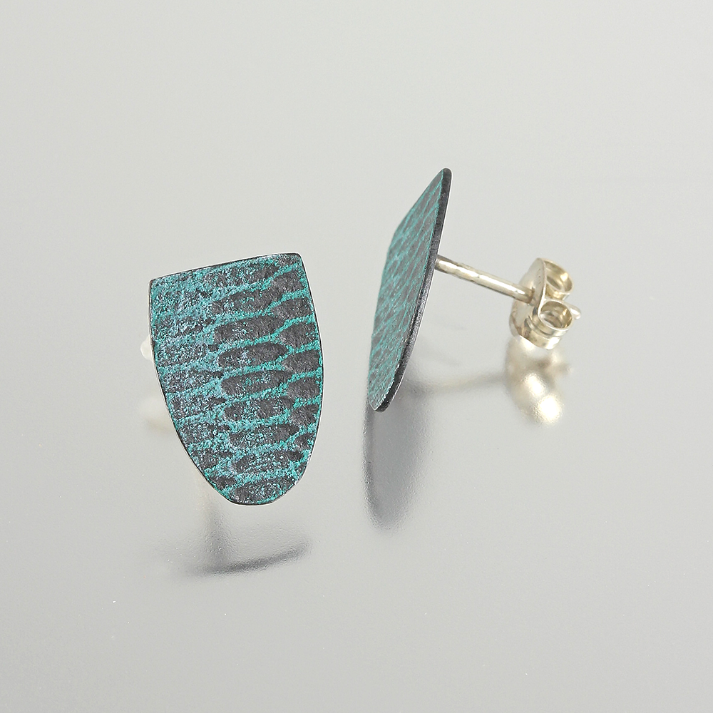 Two aqua-teal shield shaped earrings with a mod uniform snakeskin pattern on a light grey background.