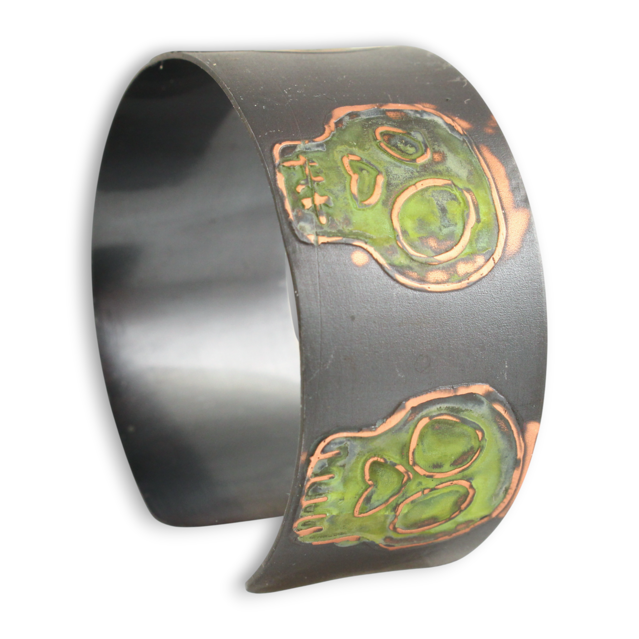 Oxidized metal cuff bracelet with green coloring over skull designs on a white background.