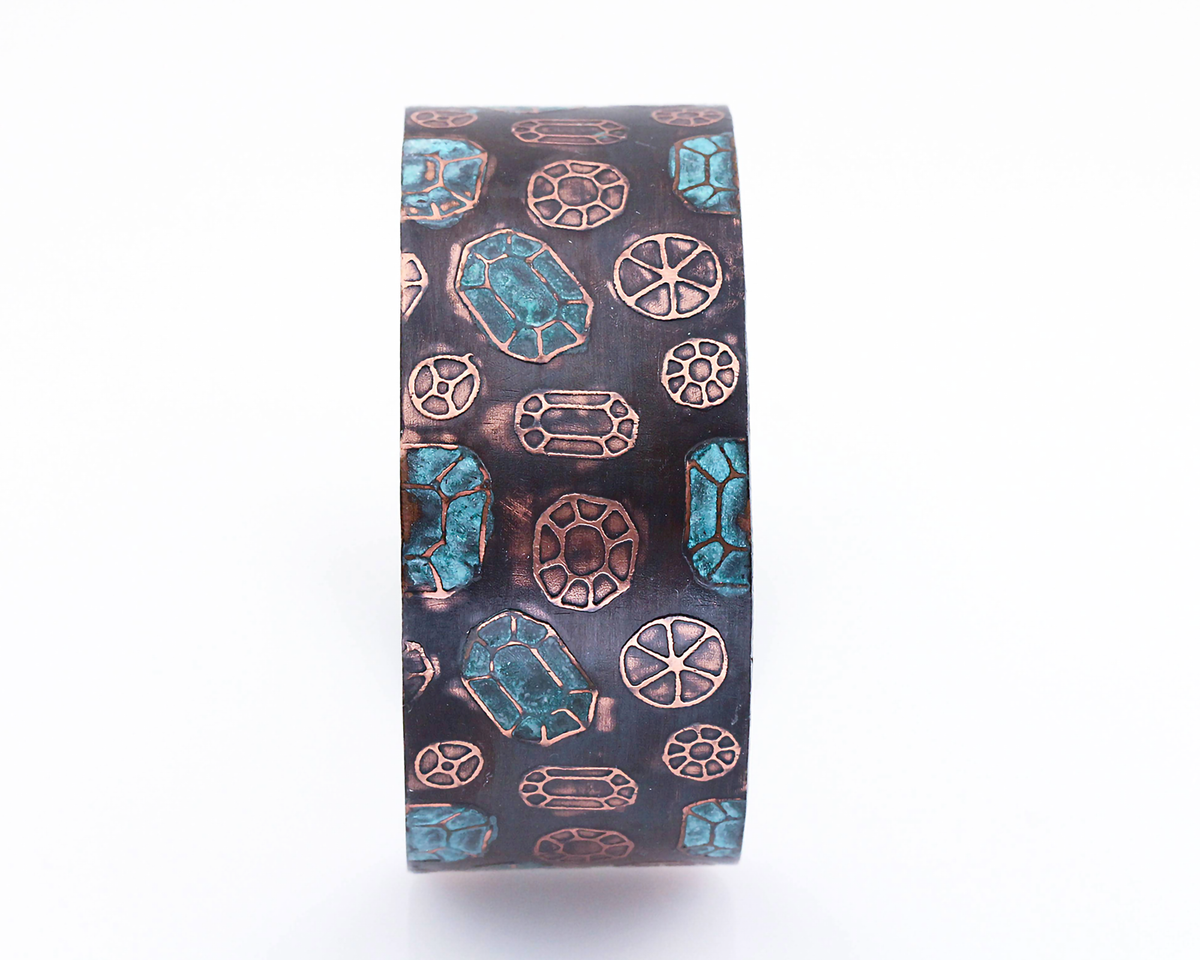 Copper cuff bracelet with gemstone pattern over the surface. Oxidized (darkened for contrast) then patinated (or coloring added) to some of the gemstones.