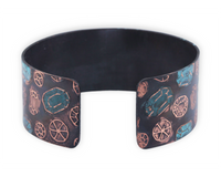 Copper cuff bracelet with gemstone pattern over the surface. Oxidized (darkened for contrast) then patinated (or coloring added) to some of the gemstones.