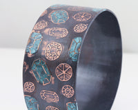 Copper cuff bracelet with gemstone pattern over the surface. Oxidized (darkened for contrast) then patinated (or coloring added) to some of the gemstones.