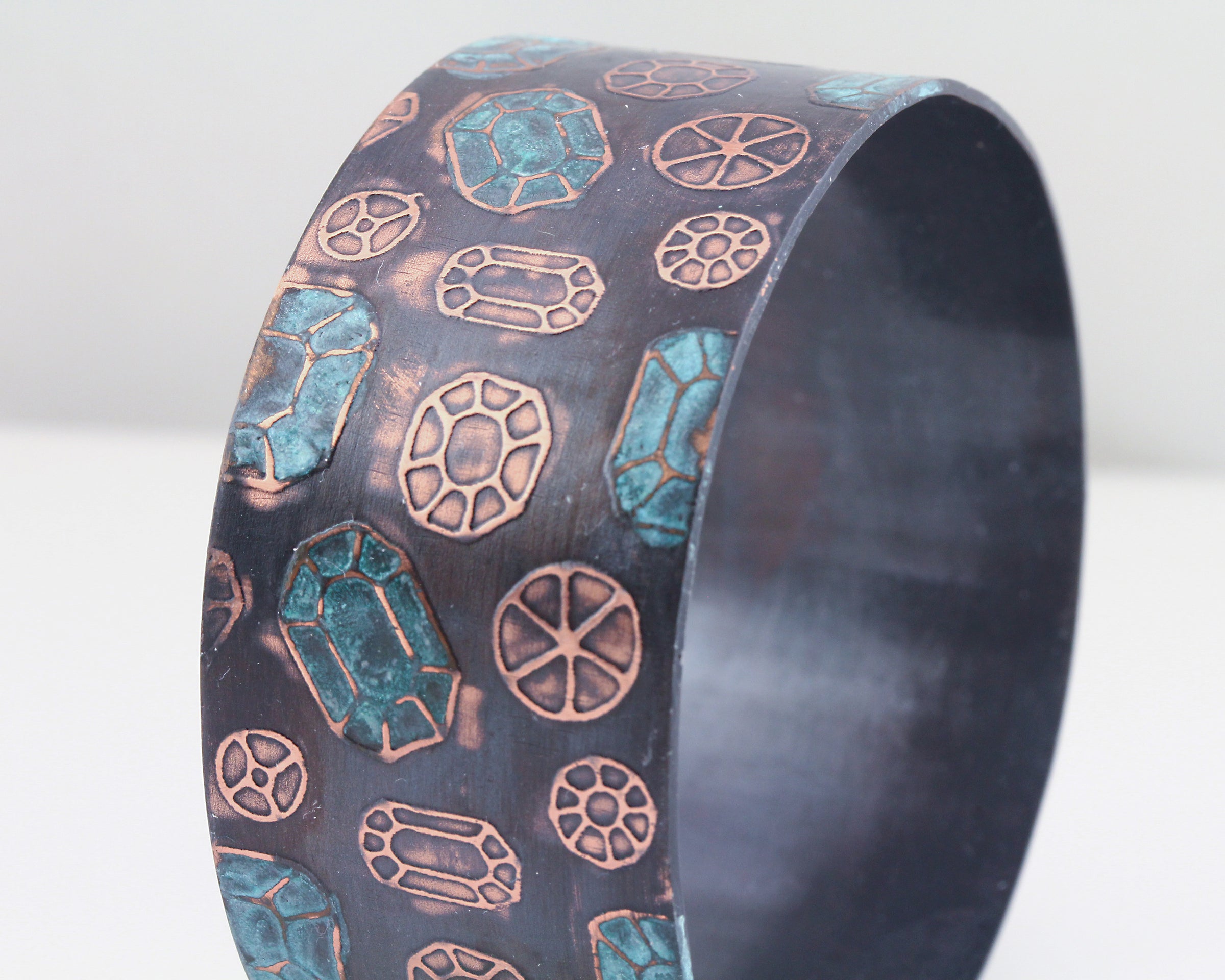 Copper cuff bracelet with gemstone pattern over the surface. Oxidized (darkened for contrast) then patinated (or coloring added) to some of the gemstones.