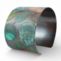 Metal cuff bracelet with green leaf pattern on a white background