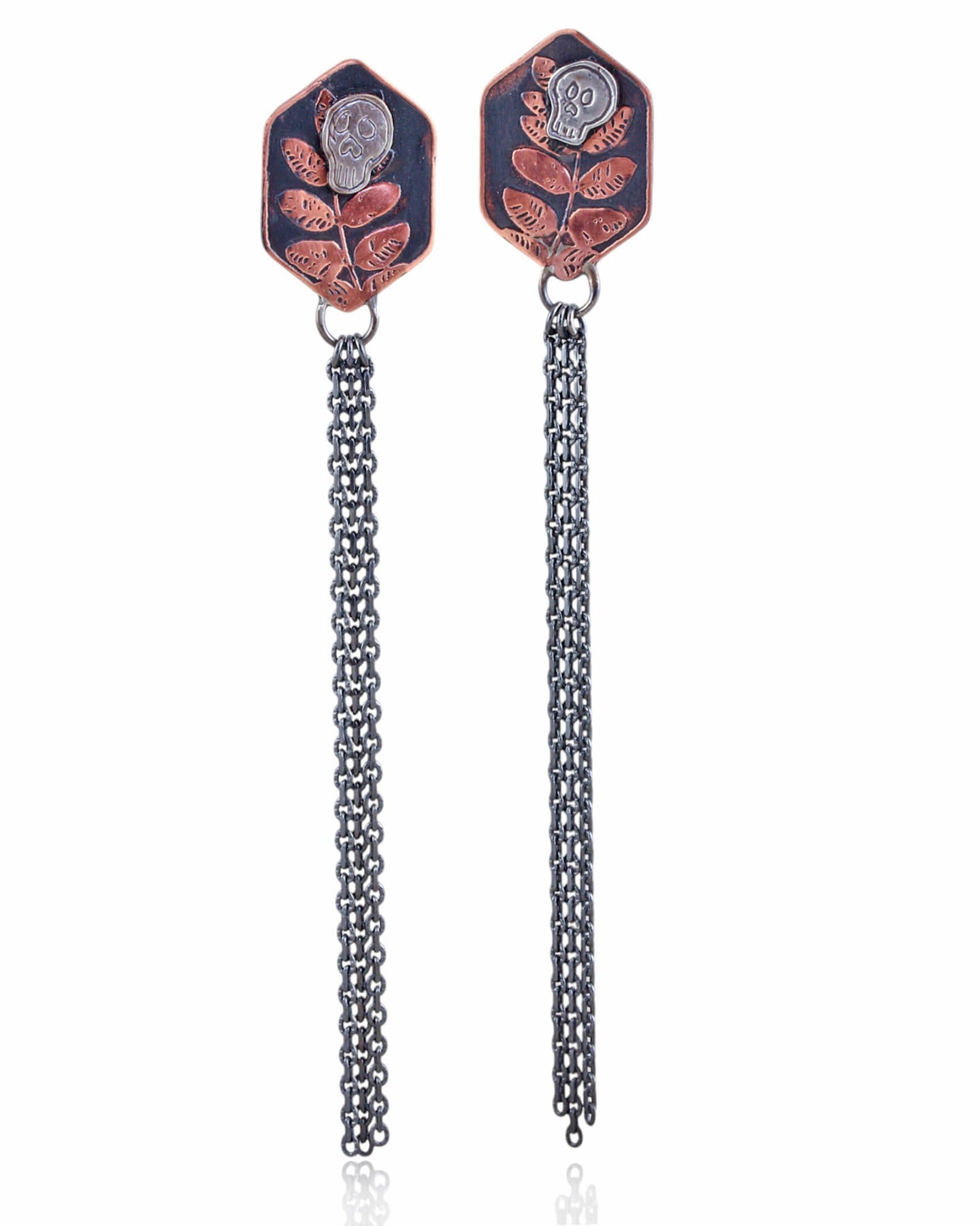 Pair of copper hexagon shaped earrings with silver skull designs and chain fringe details on a white background.