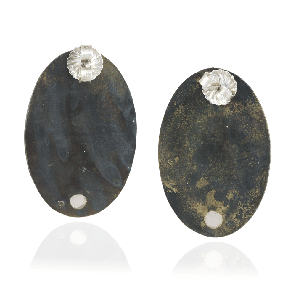 Pair of oval-shaped earrings with textured black surface and silver floral tops on a white background