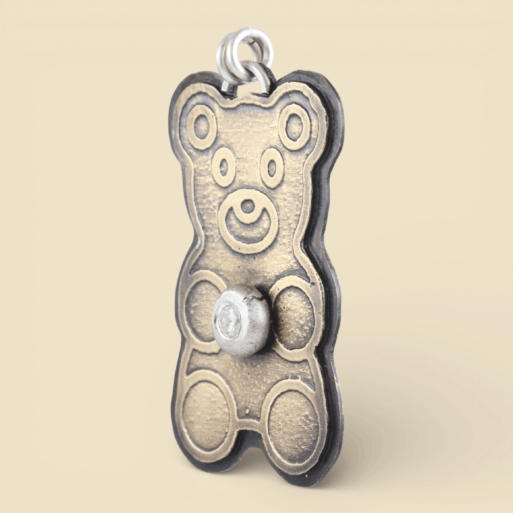 Gold teddy bear-shaped pendant with a white CZ gemstone on a beige background