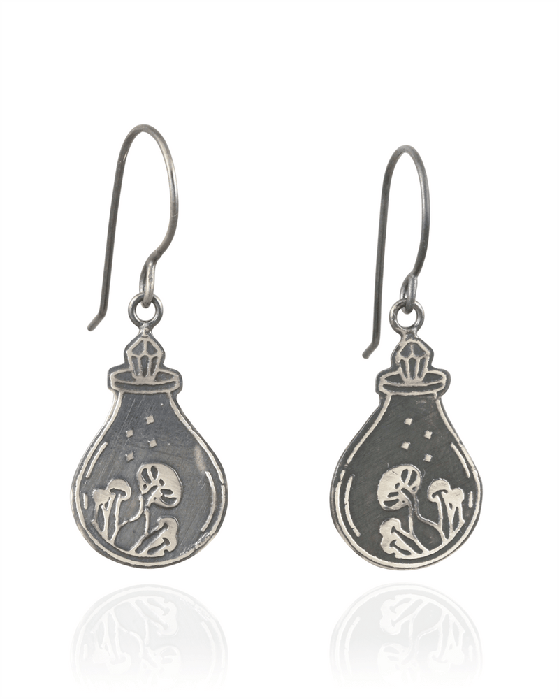 Silver earrings with a design of a potion bottle, with a crystal top, containing a mushrooms on a white background.