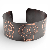 Black metal cuff bracelet with copper skull design on a white background