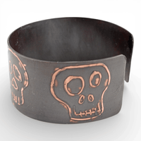Black metal cuff bracelet with copper skull design on a white background