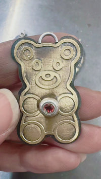 Video: Artist holding/showing nu-gold teddy bear-shaped pendant with a red ruby gemstone. by Lauren Anabela of Creative Dexterity