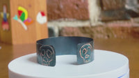 360 of a handmade copper cuff bracelet with artisan signature skull designs with blue patination on a rotating white surface.  Bracelet by Lauren Anabela of Creative Dexterity