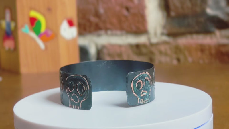 360 of a handmade copper cuff bracelet with artisan signature skull designs with blue patination on a rotating white surface.  Bracelet by Lauren Anabela of Creative Dexterity