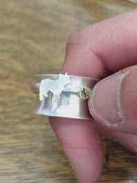 Video of a smaller silver ring with a french bulldog silhouette with a tennis ball before it being spun on a wider ring band. 