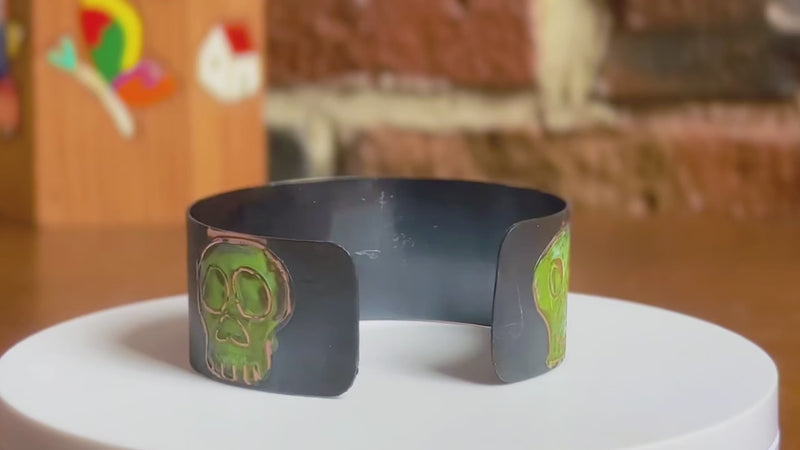 360 of a handmade copper cuff bracelet with artisan signature skull designs with green patination on a rotating white surface.  Bracelet by Lauren Anabela of Creative Dexterity