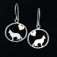 Sterling silver German Shepherd dangle earrings with a small copper heart inside oval frames, matte finish on black background.