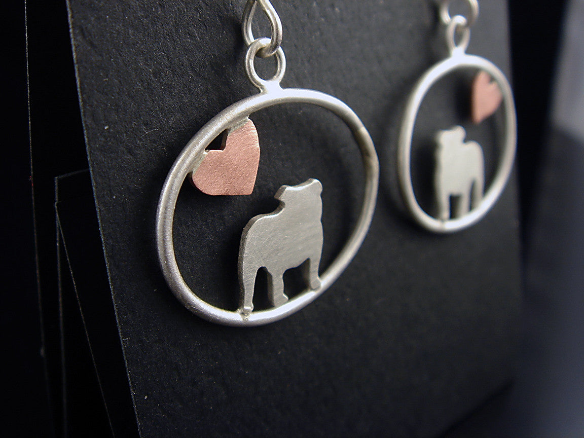 Sterling silver English Bulldog dangle earrings with copper heart inside oval frame, matte finish on black backgrounded car.