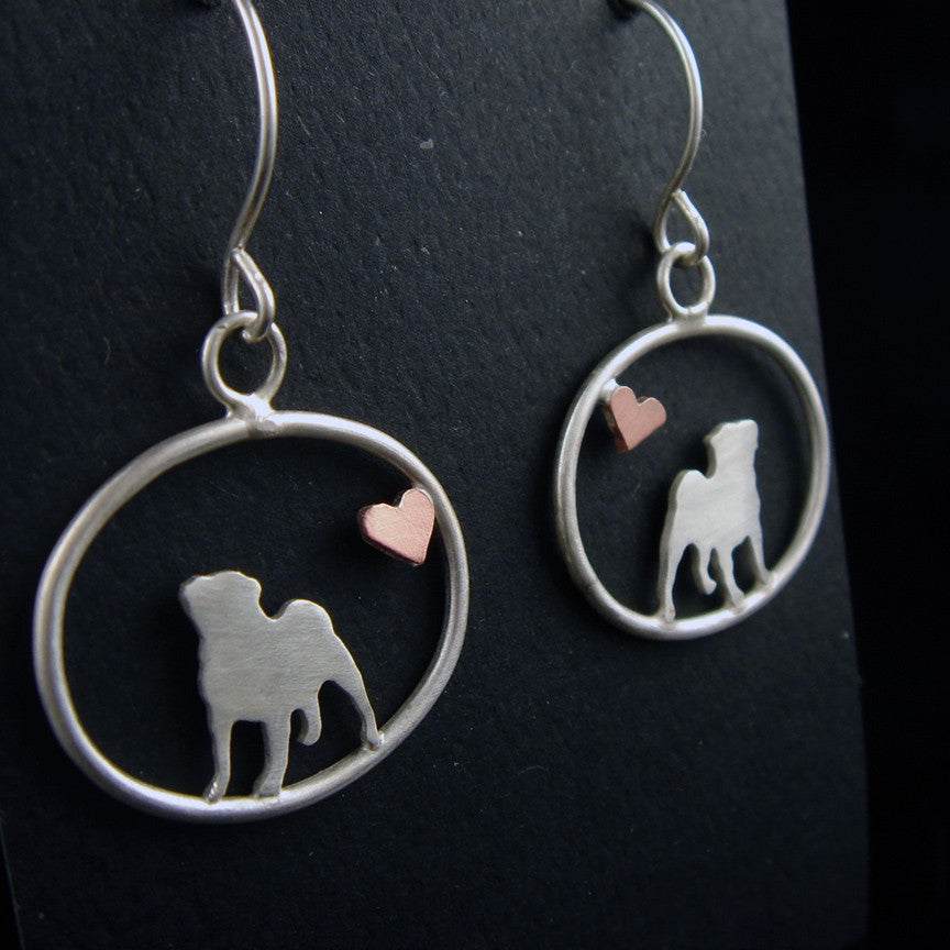 Sterling silver Pug dangle earrings with a small copper heart inside oval frames, matte finish on black background.