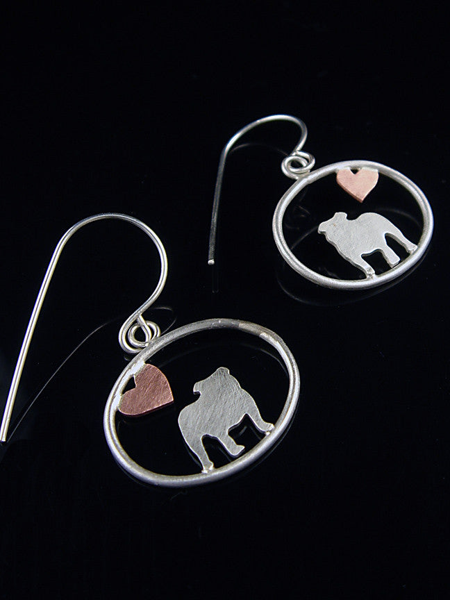 Sterling silver English Bulldog dangle earrings with copper heart inside oval frame, matte finish on reflective black background.