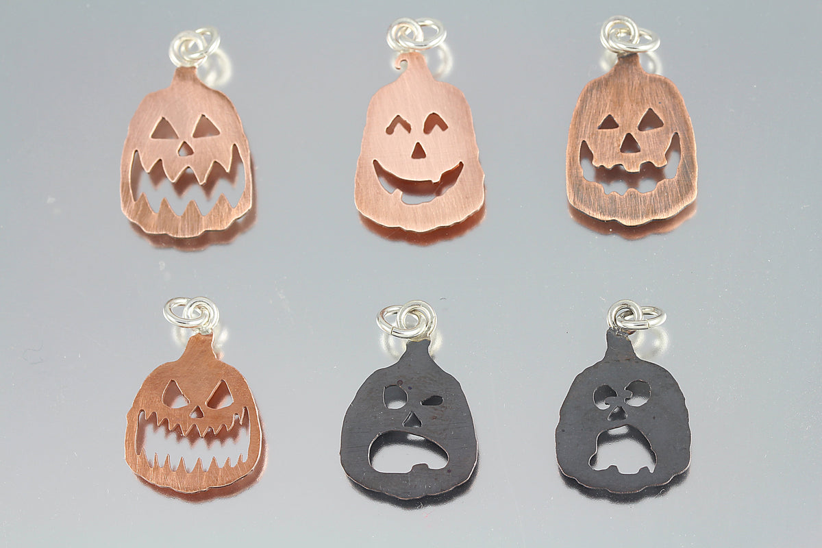 Hand-cut copper Halloween pumpkin pendants with sterling silver jump rings, featuring detailed carved faces in both bright and antiqued finishes.